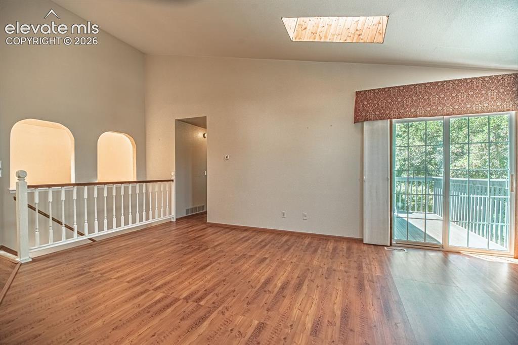 Image 19 of 36: Spacious room with wood-finish flooring, a skylight, and an arched hallway