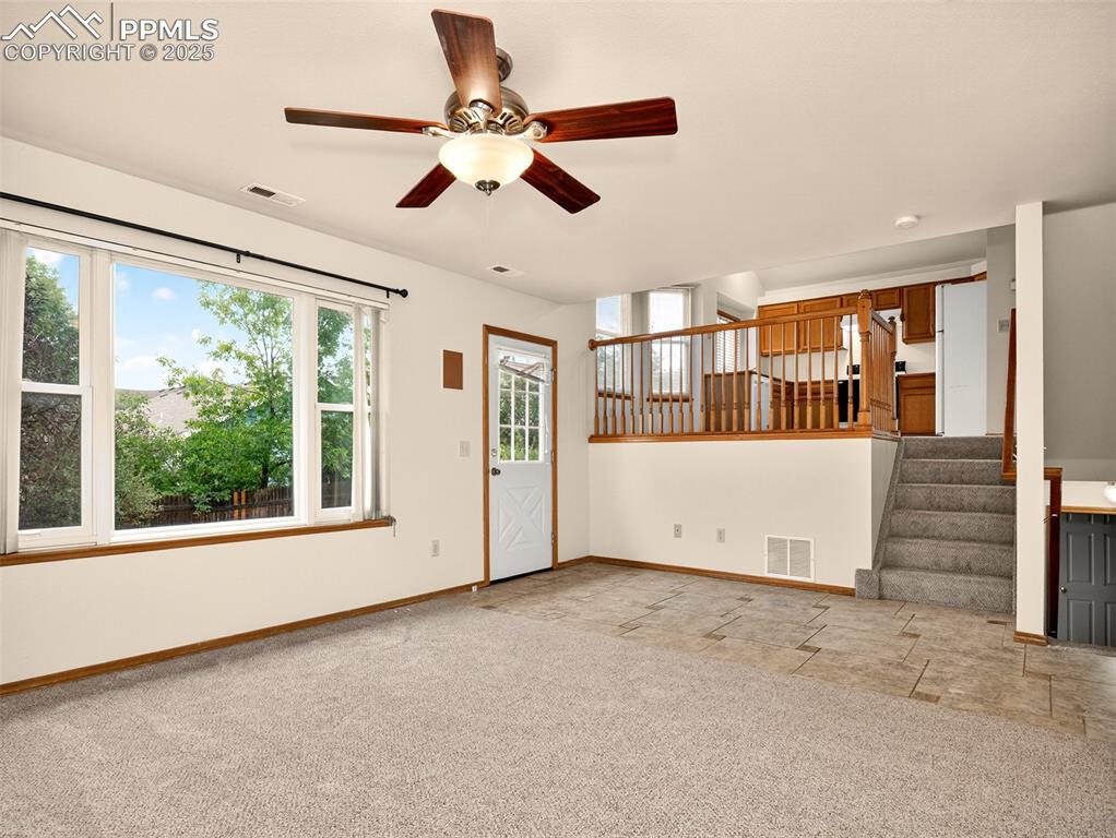Image 12 of 26: Unfurnished living room featuring stairway, light carpet, and a ceiling fan