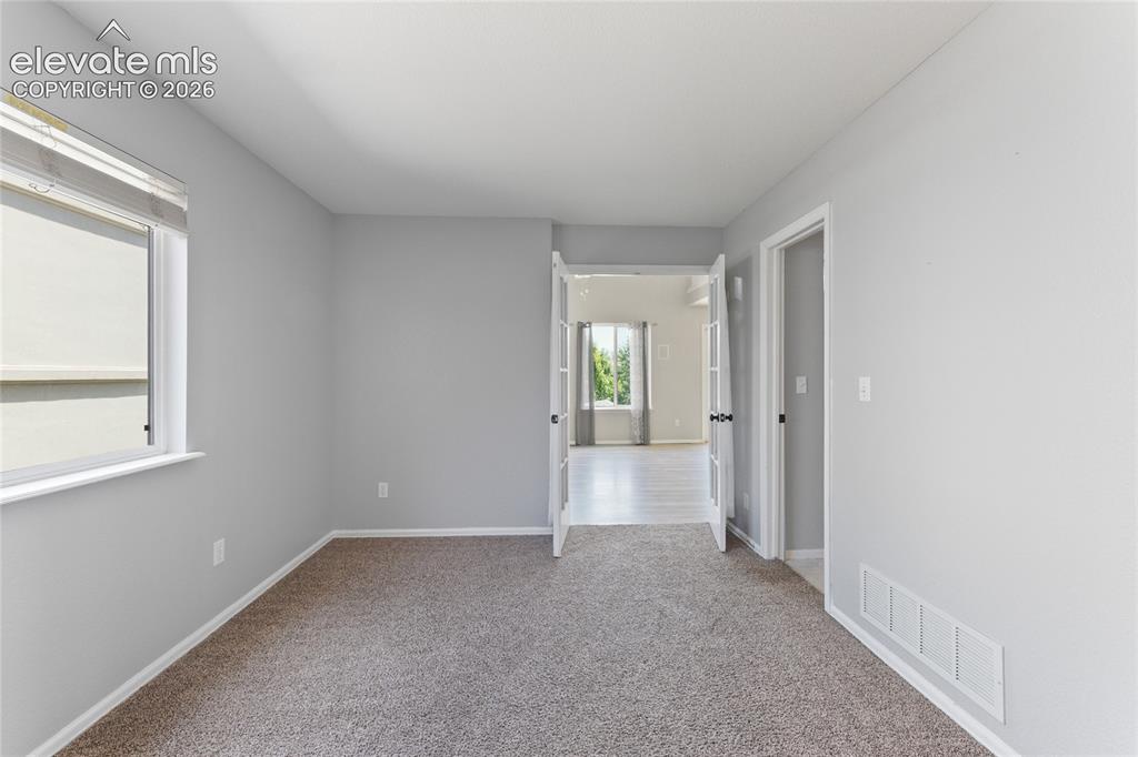Image 14 of 36: Interior room featuring neutral-toned carpet, a single window with blinds, 