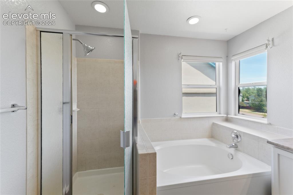 Image 24 of 36: Full-size soaking tub with tiled surround and two windows