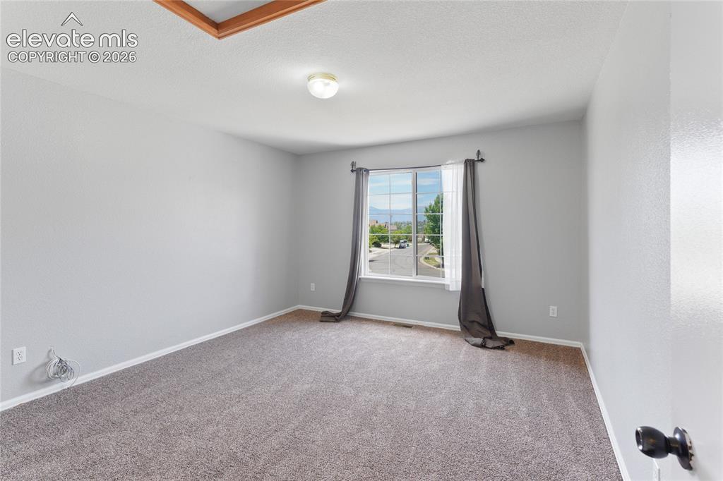 Image 26 of 36: Bright room featuring a large window, neutral gray walls, and plush carpeti