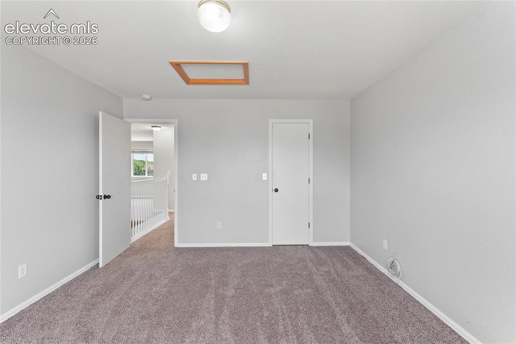 Image 27 of 36: Carpeted room with a ceiling-mounted light fixture and an attic access pane