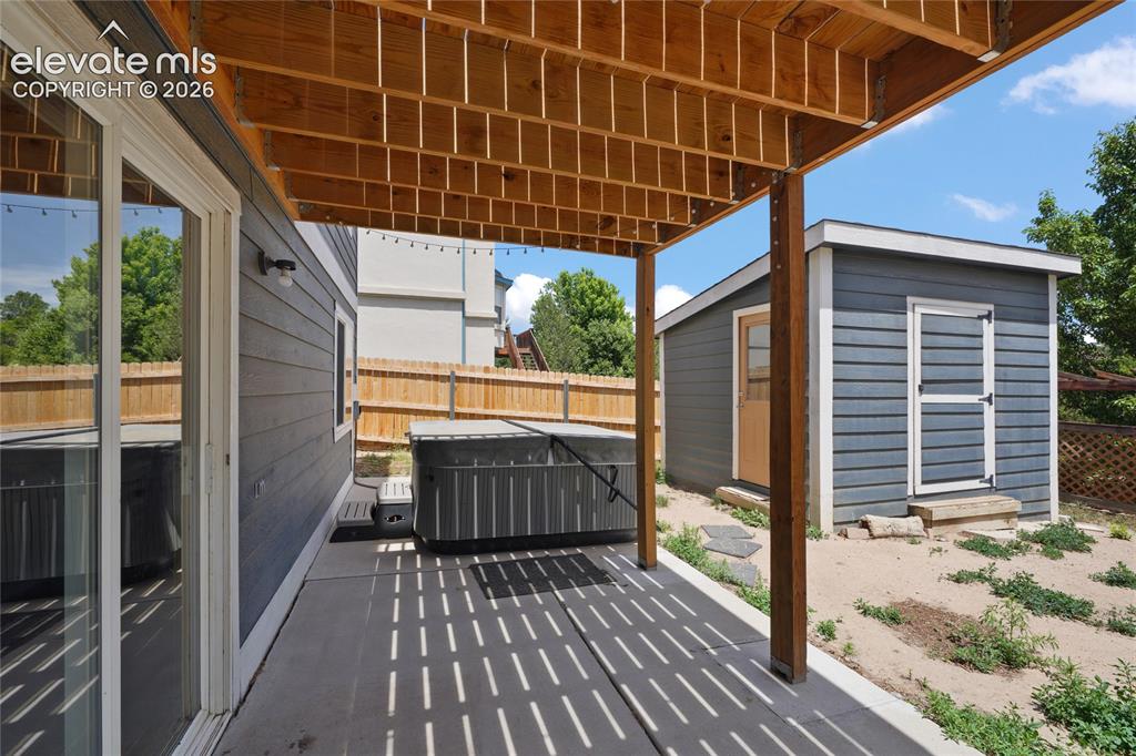Image 34 of 36: Covered patio featuring a hot tub, string lighting, and a wood privacy fenc
