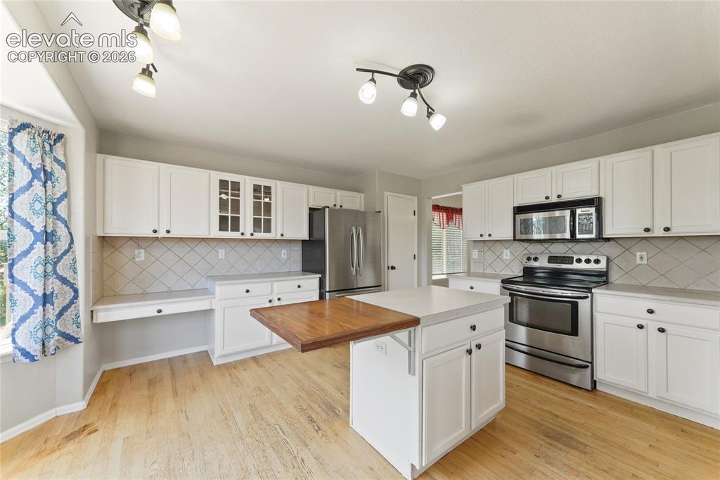 Image 9 of 36: Kitchen featuring wood-finish flooring, white cabinetry, stainless steel ap