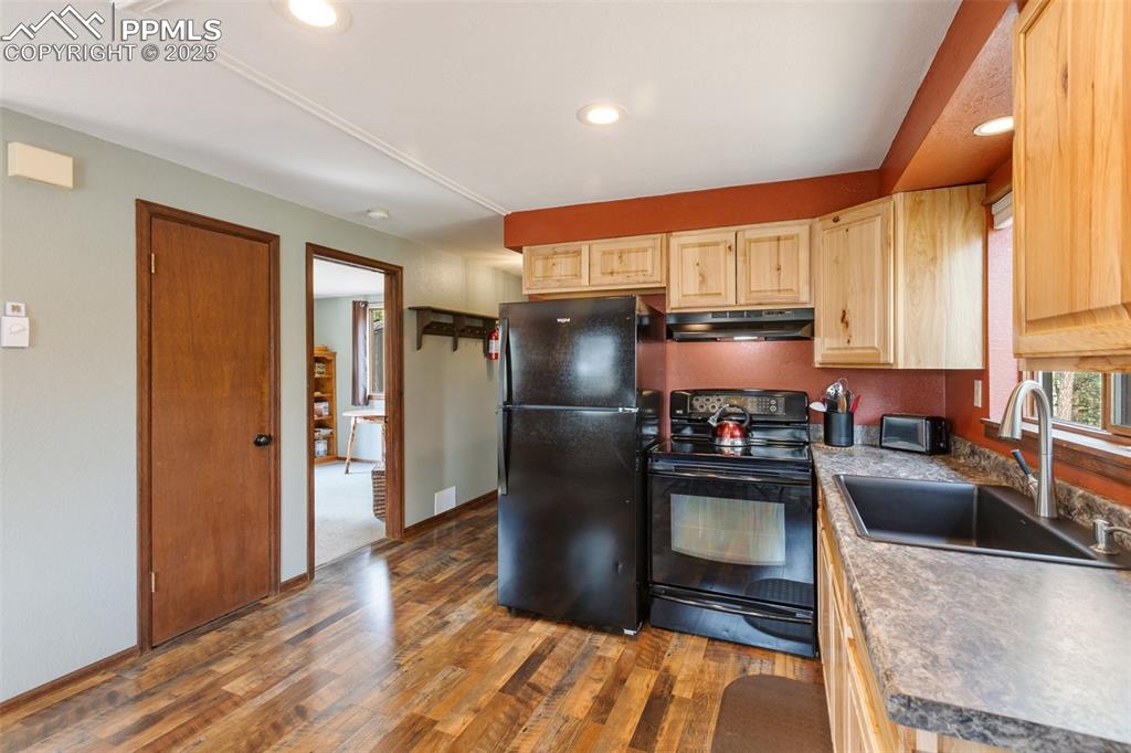 Image 15 of 50: Kitchen with black appliances, dark wood finished floors, light brown cabin