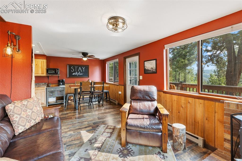 Image 6 of 50: Living room with wood finished floors, a baseboard heating unit, ceiling fa