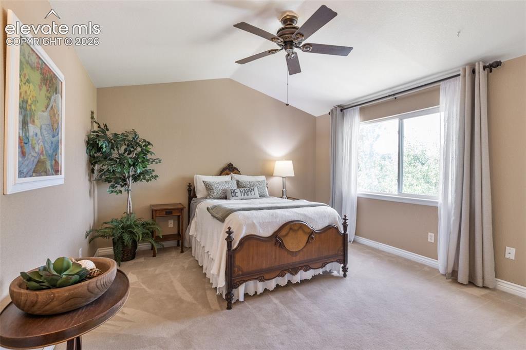 Image 20 of 47: Generous primary bedroom with vaulted ceiling, fan, and carpet flooring.