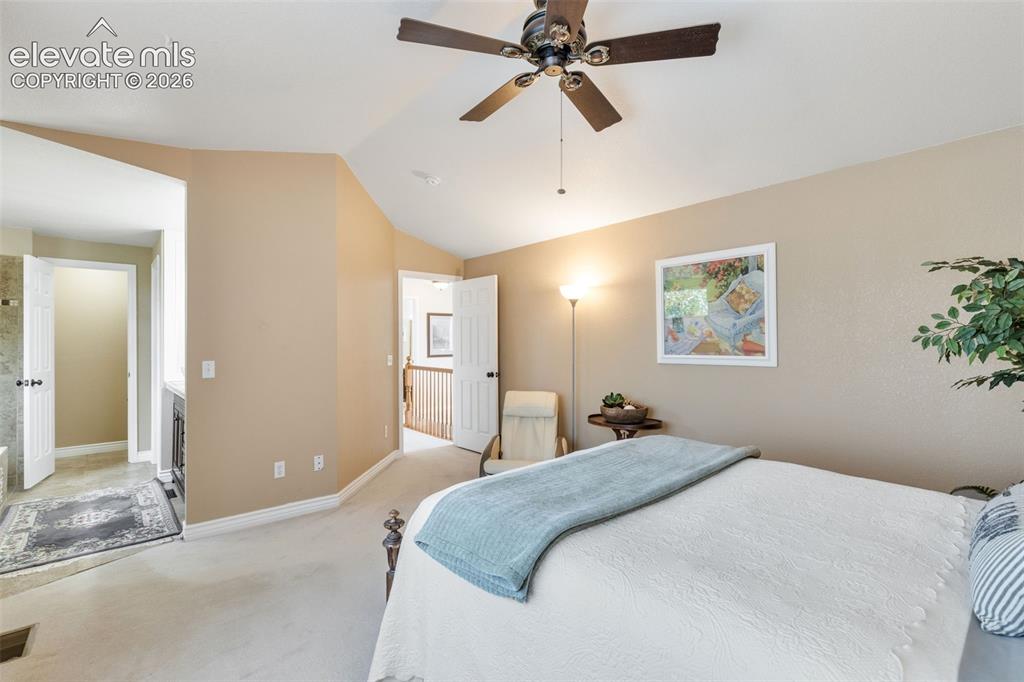 Image 21 of 47: Generous primary bedroom with vaulted ceiling, fan, and carpet flooring. 