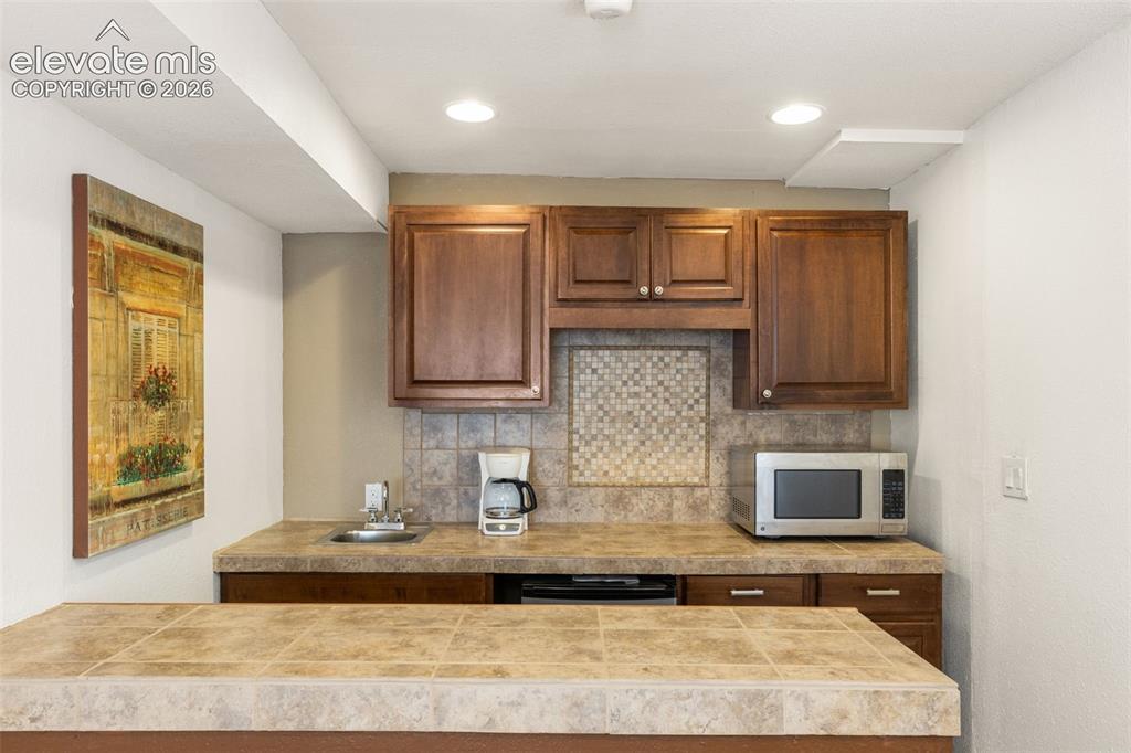 Image 30 of 47: Wet bar with sink and dishwasher, tiled countertops and storage.