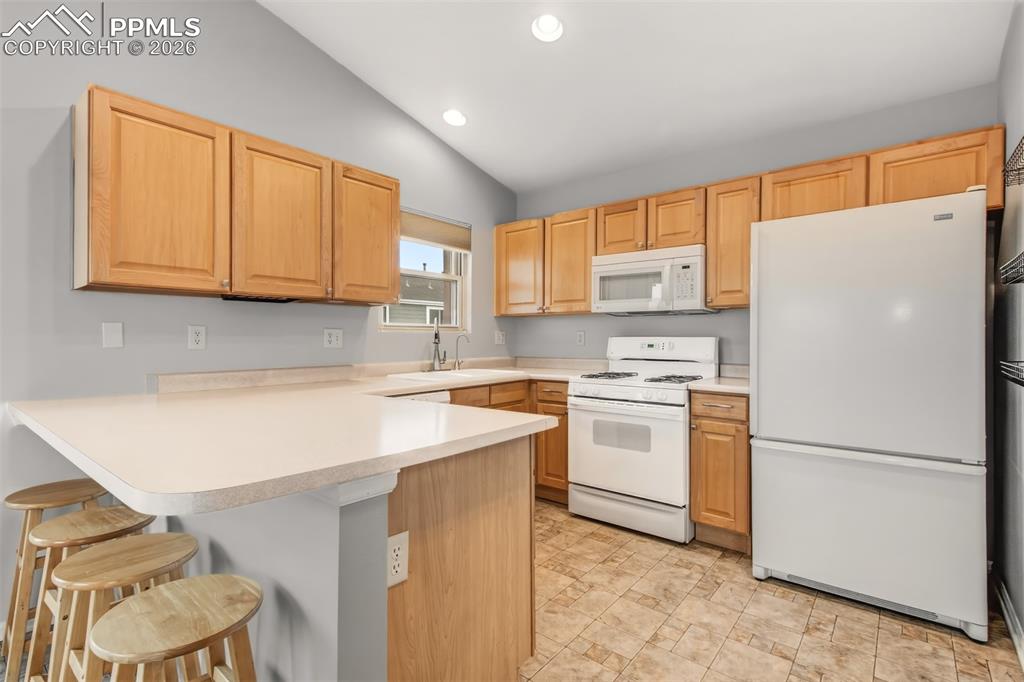 Image 6 of 27: Kitchen featuring white appliances, a breakfast bar area, a peninsula, ligh