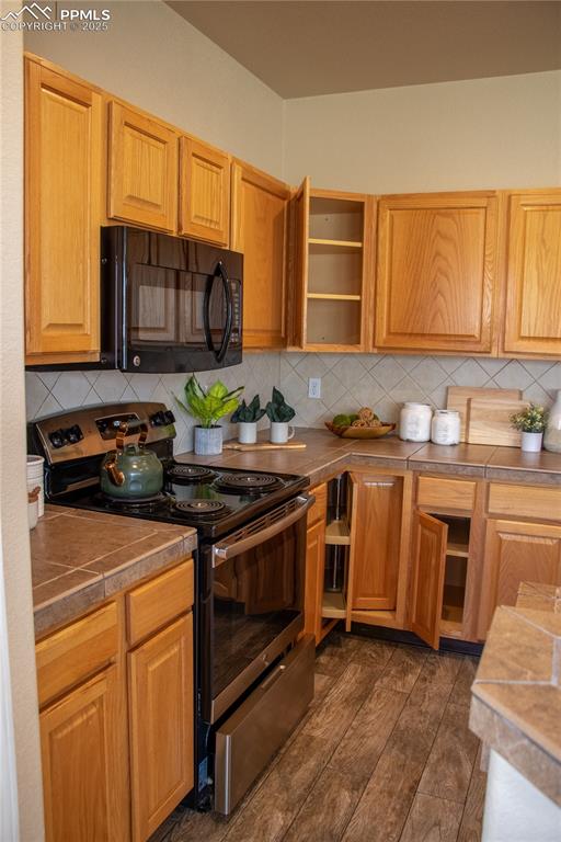 Image 10 of 31: Kitchen with electric stove, black microwave, backsplash, tile counters, an