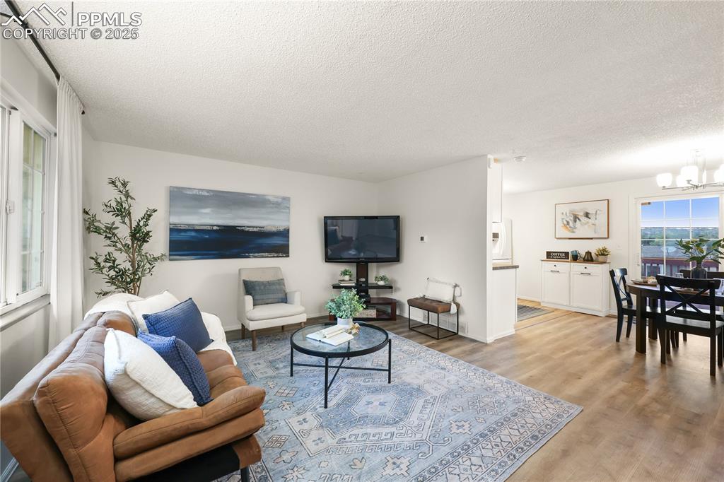Image 4 of 32: Living area with light wood-type flooring, a textured ceiling, and a chande