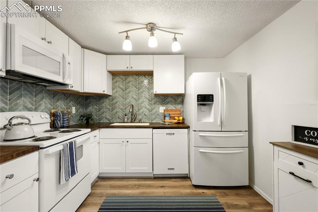 Image 9 of 32: Kitchen with white appliances, tasteful backsplash, white cabinetry, butche