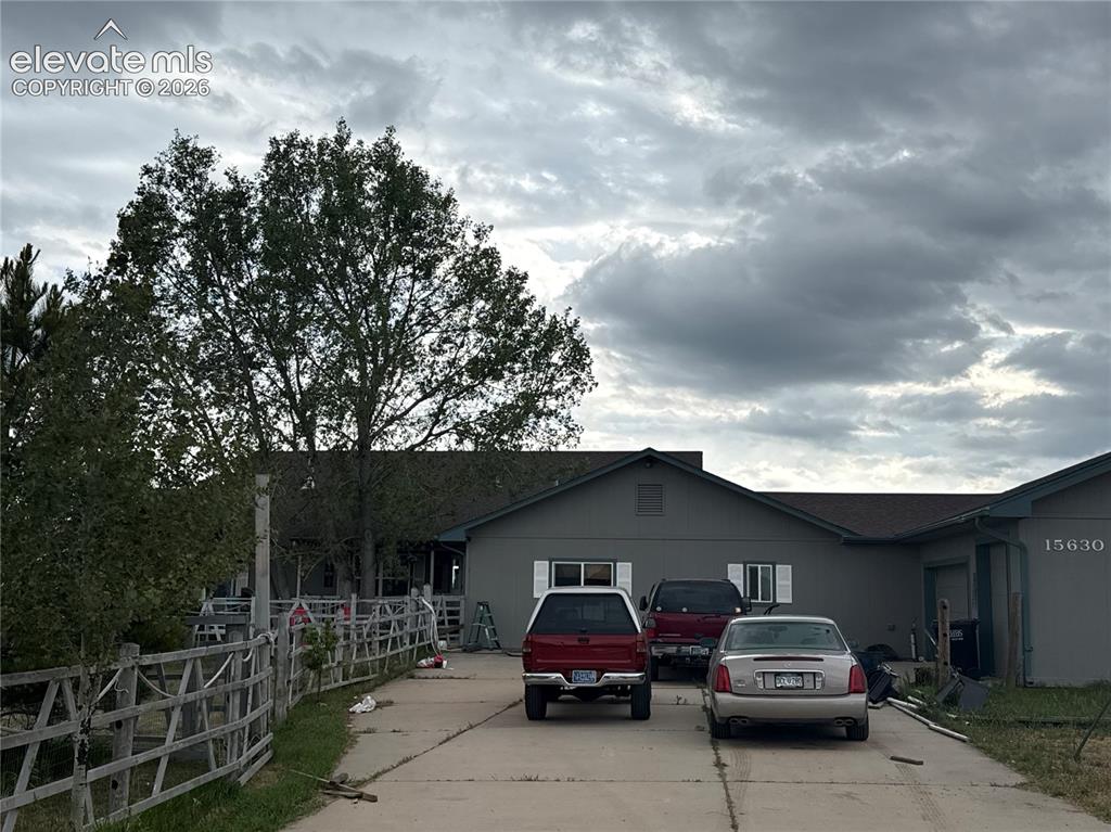 Caption: Ranch-style exterior with a paved driveway, wood fencing, and mature trees
