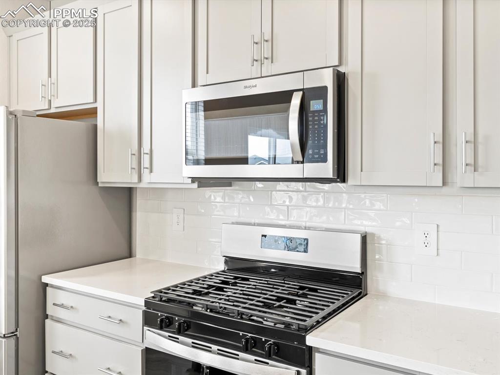 Image 9 of 43: Kitchen with decorative backsplash, light stone countertops, white cabinetr