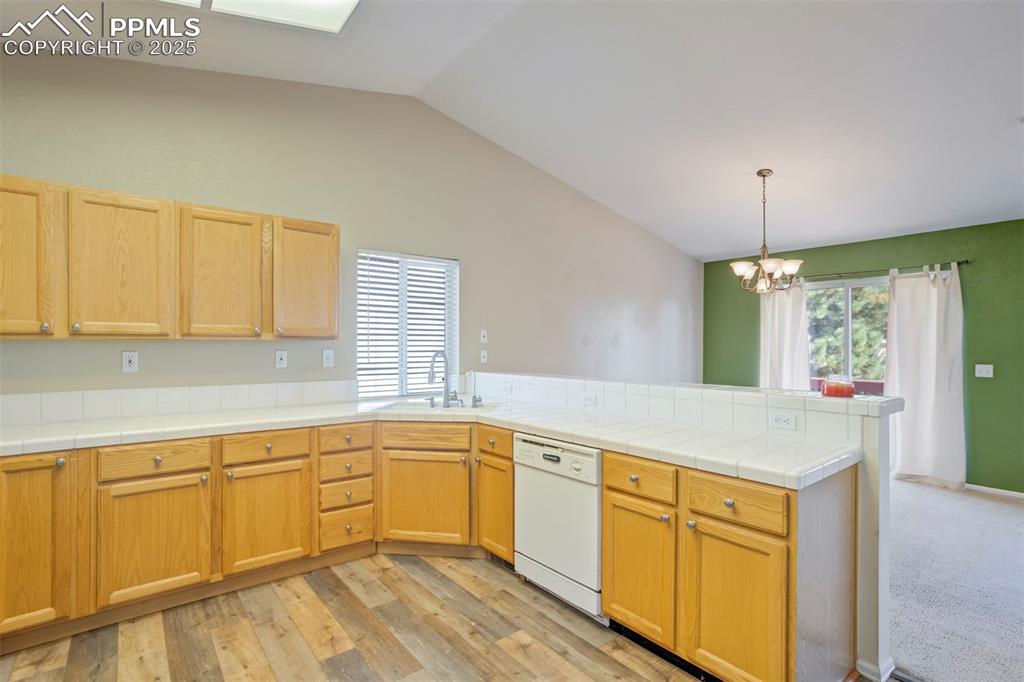 Image 15 of 50: Kitchen with a peninsula, vaulted ceiling, tile countertops, dishwasher, an