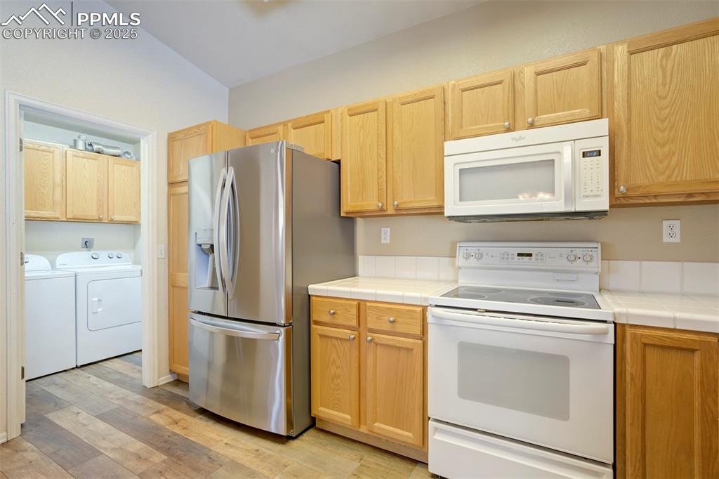 Image 17 of 50: Kitchen with white appliances, light wood finished floors, washing machine 