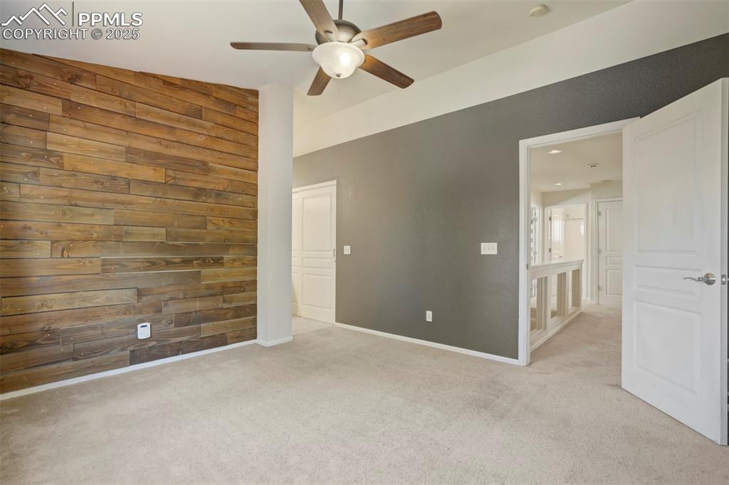 Image 19 of 50: Unfurnished bedroom featuring wooden walls, carpet floors, and a ceiling fa