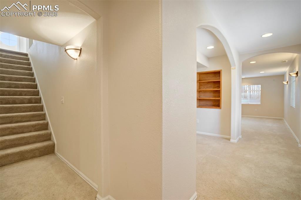Image 33 of 50: Corridor with light carpet, arched walkways, stairway, and recessed lightin