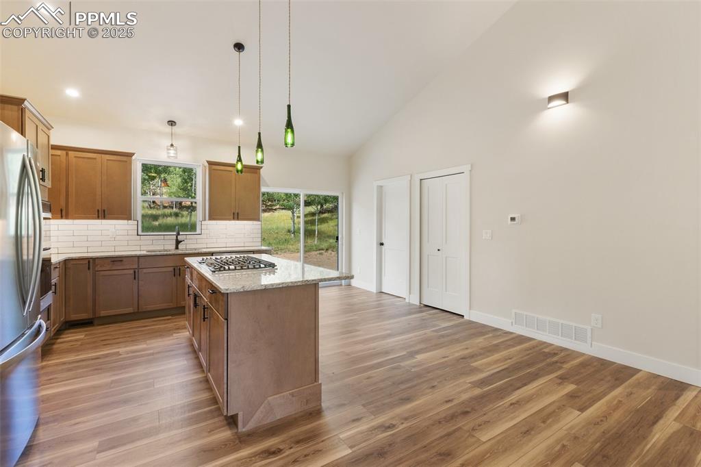 Image 10 of 35: Kitchen featuring brown cabinets, a kitchen island, tasteful backsplash, hi