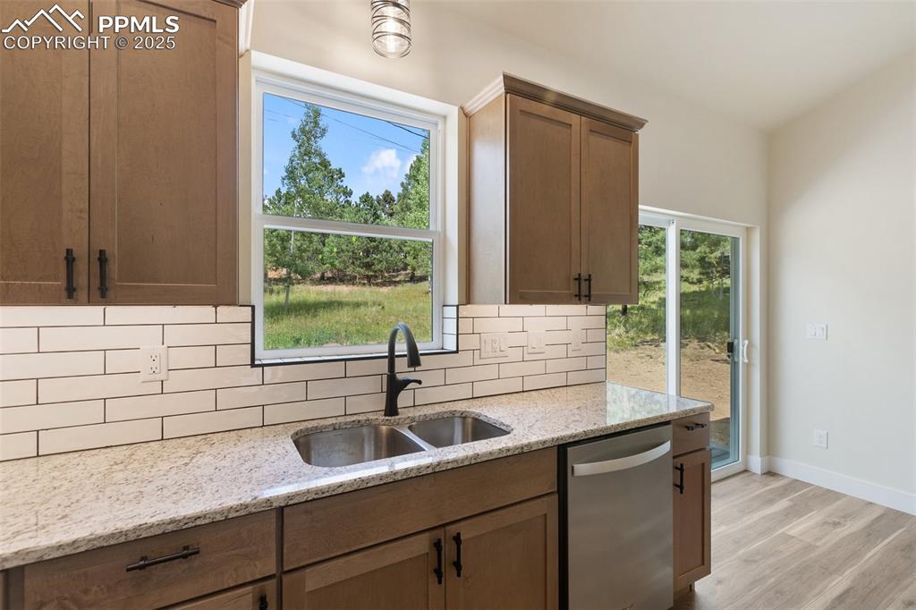 Image 16 of 35: Kitchen featuring backsplash, dishwasher, light stone countertops, light wo