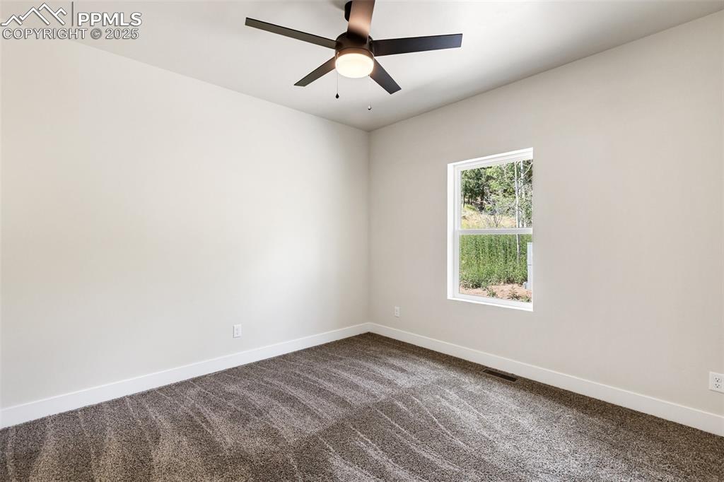 Image 32 of 35: Empty room with dark colored carpet and a ceiling fan