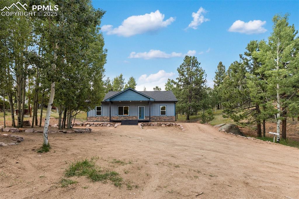 Image 7 of 35: Back of house with a porch, stone siding, dirt driveway, and board and batt