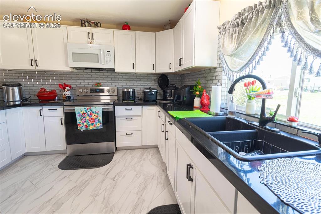 Image 20 of 25: Kitchen featuring electric range, white microwave, a sink, dark countertops