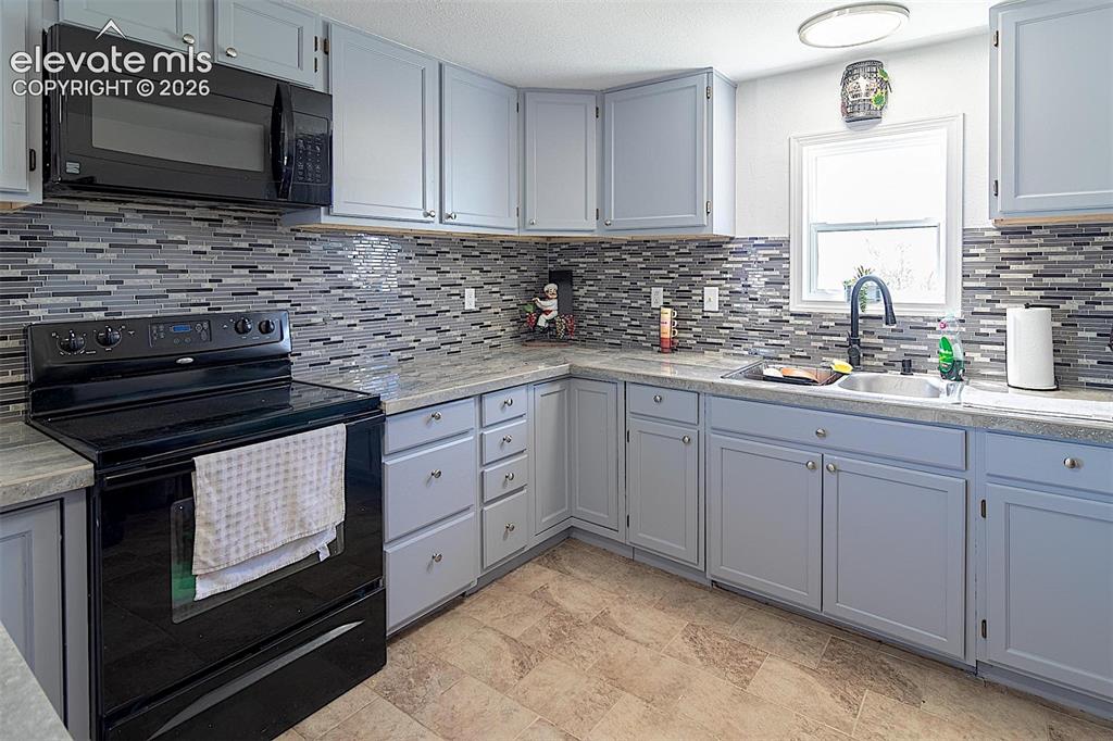 Image 5 of 25: Kitchen with black appliances, a sink, decorative backsplash, and light cou