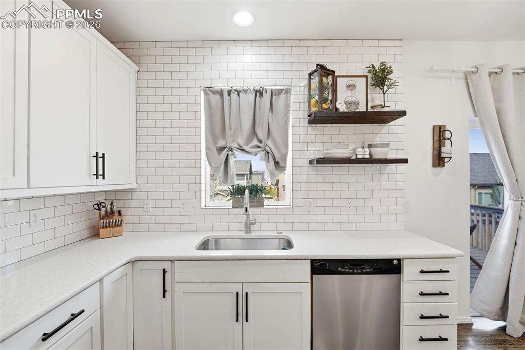 Image 16 of 48: Kitchen with white cabinets, dishwasher, open shelves, and light stone coun
