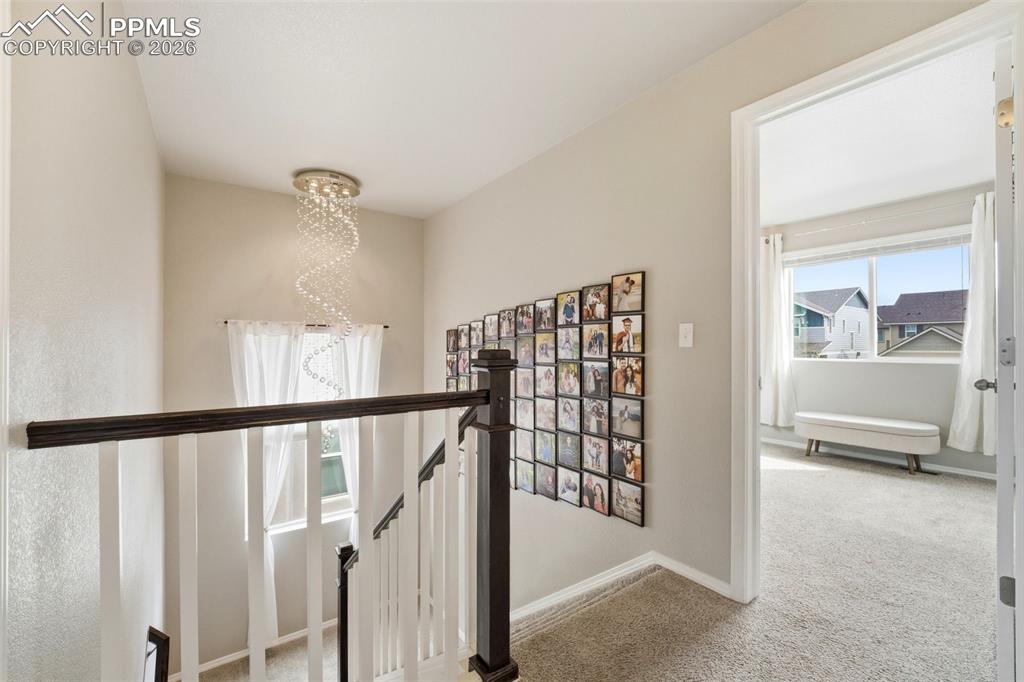 Image 23 of 48: Hall featuring light carpet, suspended lighting, and an upstairs landing