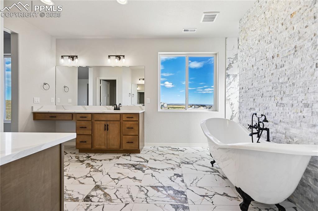 Image 11 of 36: Bathroom with vanity, a freestanding bath, light marble finish flooring, an
