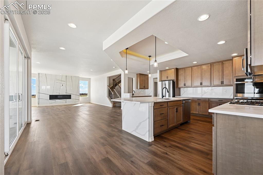 Image 22 of 36: Kitchen featuring hanging light fixtures, brown cabinetry, a raised ceiling