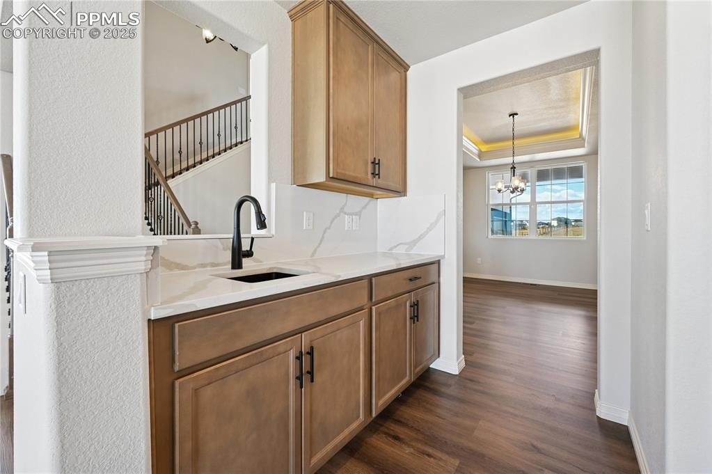 Image 25 of 36: Bar area with a raised ceiling, light stone countertops, dark wood-type flo