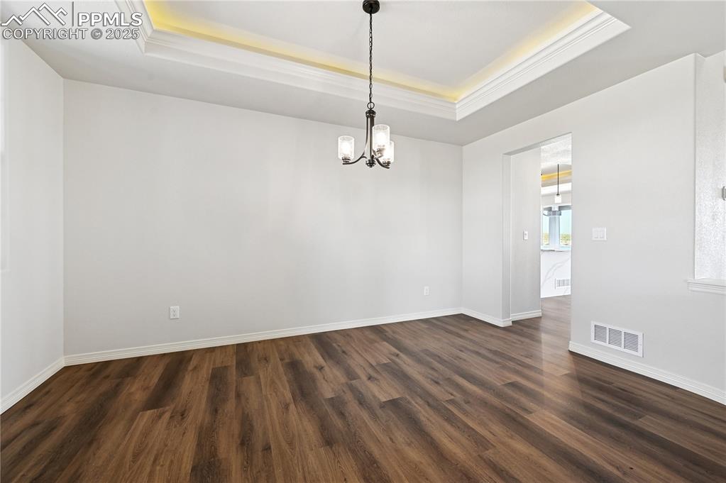 Image 32 of 36: Unfurnished room featuring a tray ceiling, dark wood-style flooring, a chan