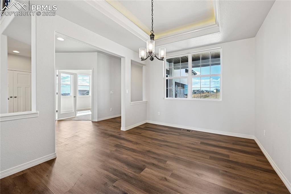 Image 34 of 36: Unfurnished dining area with a raised ceiling, dark wood-type flooring, and
