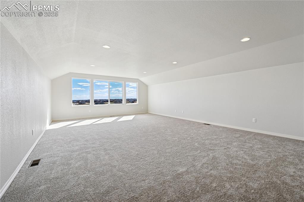 Image 9 of 36: Additional living space with vaulted ceiling, carpet floors, a textured cei