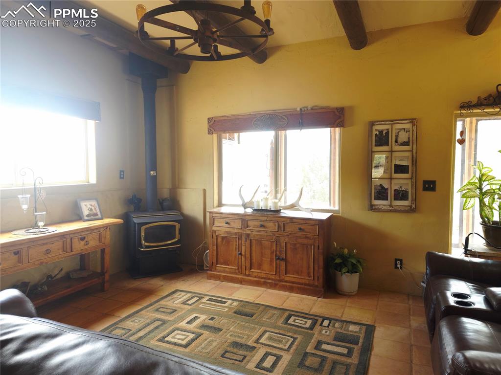 Image 11 of 42: Living room with a wood stove, light tile patterned flooring, and beam ceil