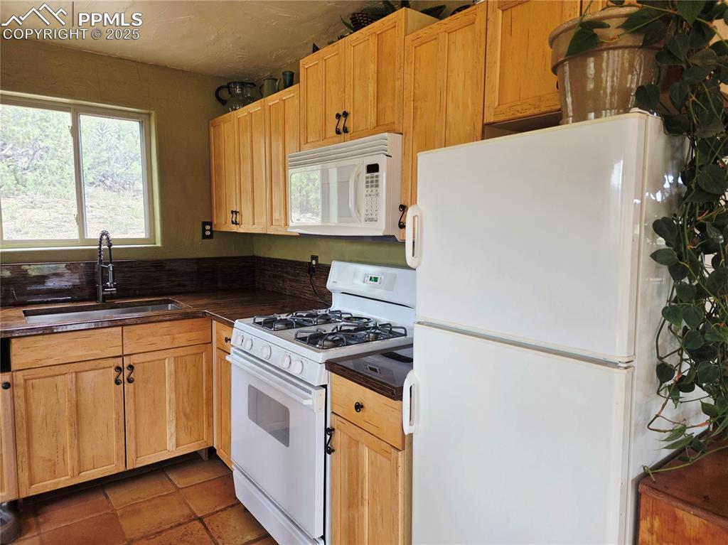 Image 8 of 42: Kitchen featuring white appliances, dark countertops, light brown cabinetry