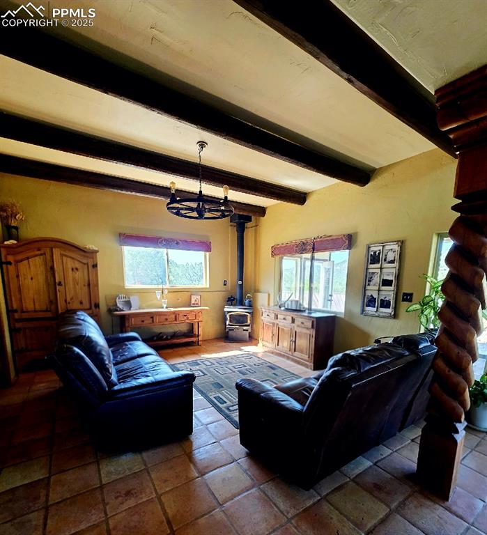 Image 9 of 42: Living room with beam ceiling, a chandelier, and a wood stove