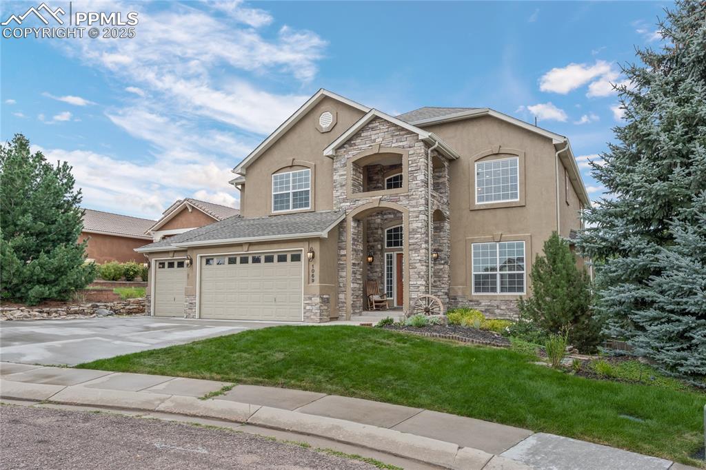 Caption: View of front facade featuring stone siding, stucco siding, a front yard, and driveway