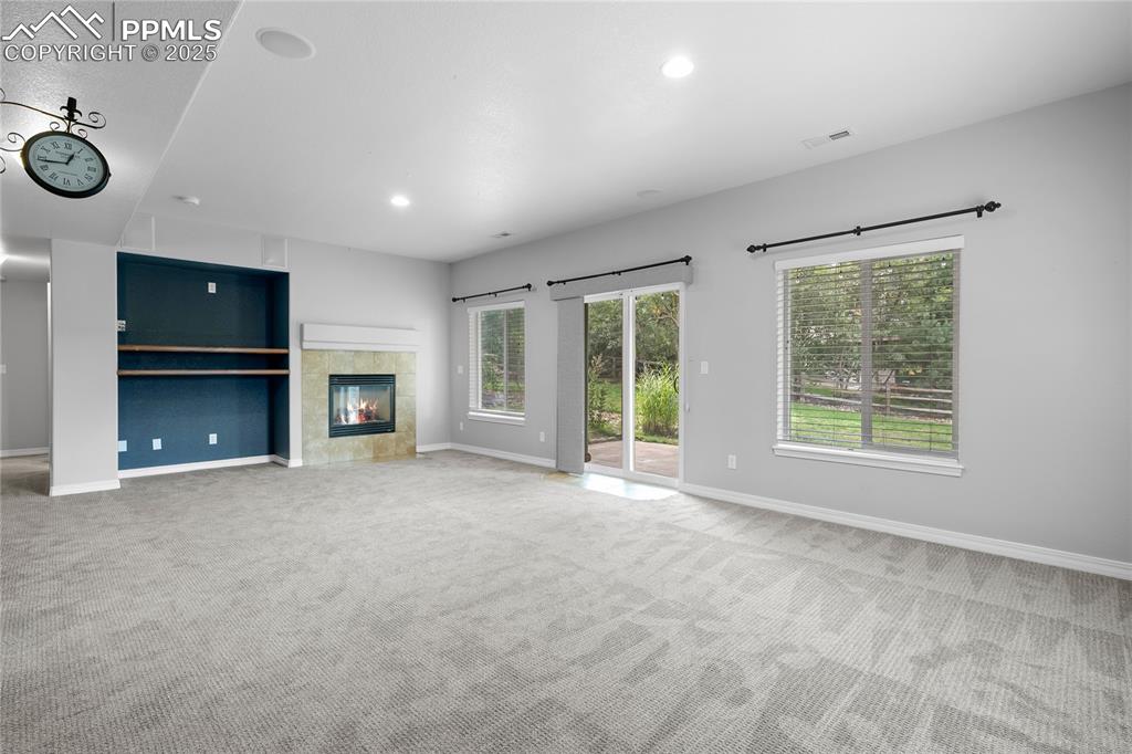 Image 18 of 24: Basement family room featuring a tile fireplace, carpet, plenty of natural 