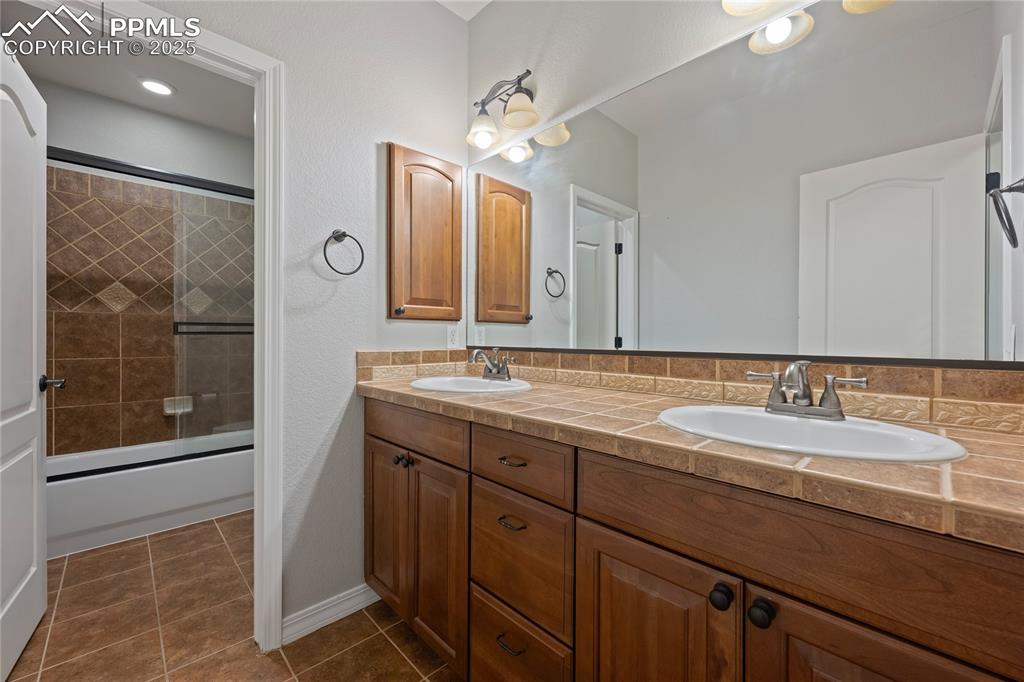 Image 21 of 24: Basement Bathroom with bath / shower combo with glass door, dark tile patte
