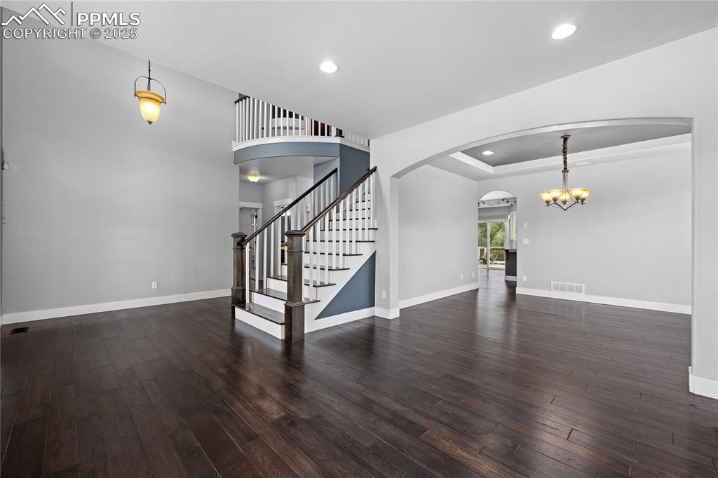 Image 4 of 24: Living room with dark wood-type flooring, stairway, chandelier, recessed li
