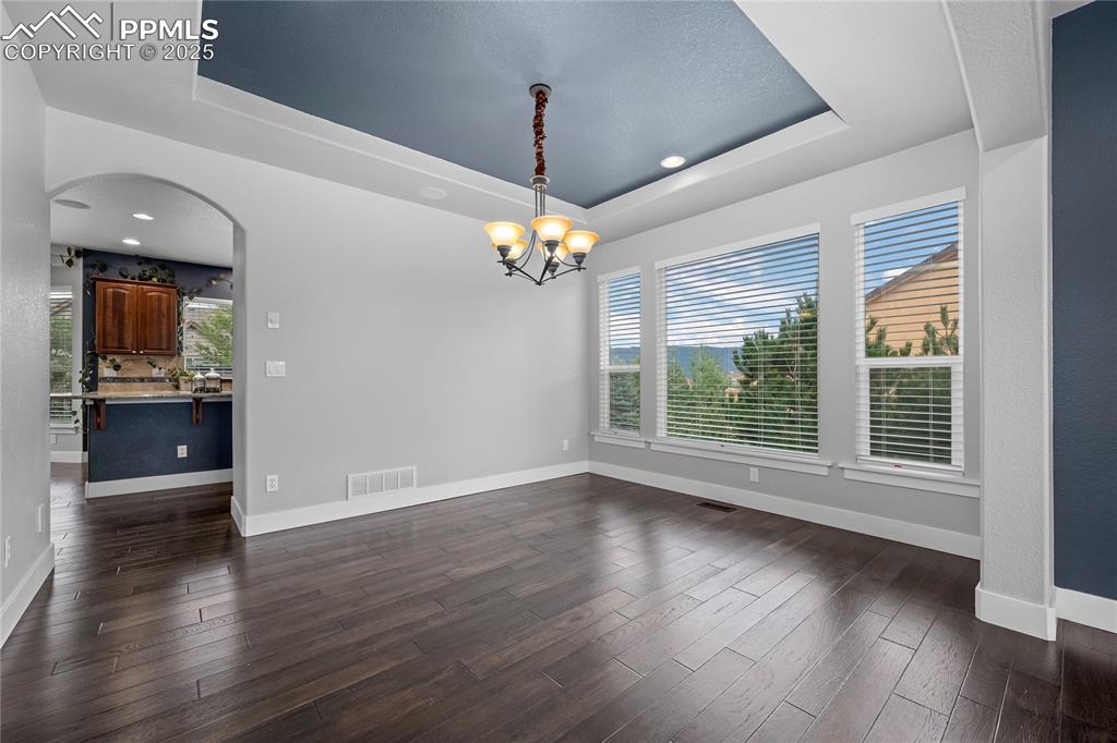 Image 5 of 24: Dining area featuring a tray ceiling, dark wood-style floors, arched walkwa