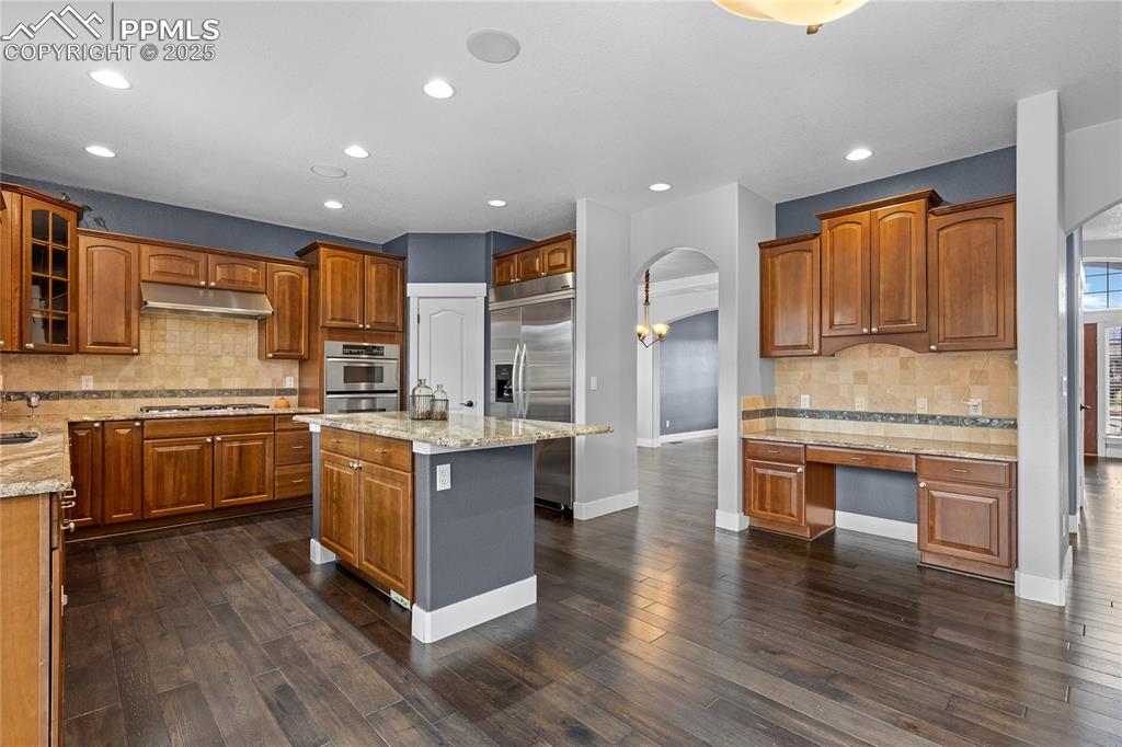 Image 7 of 24: Kitchen with decorative backsplash, arched walkways, brown cabinetry, a cen