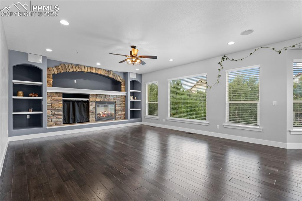Image 8 of 24: Unfurnished living room with built in features, a stone fireplace, dark woo