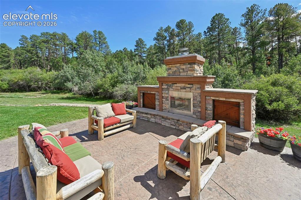 Image 37 of 48: Outdoor wood furniture at fireplace conveys!