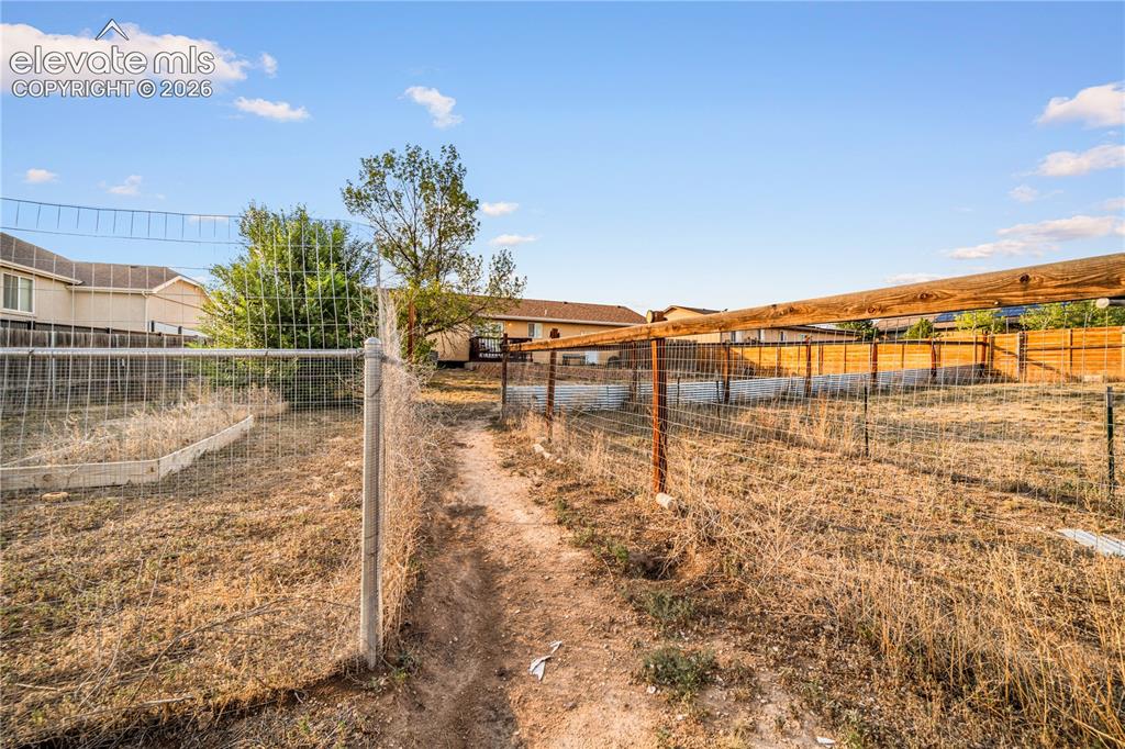Image 18 of 20: Expansive backyard featuring a chain-link fence, a dirt path, and a wooden 