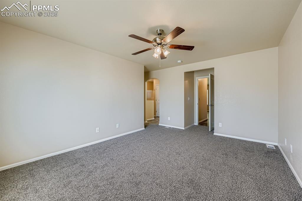 Image 14 of 26: Unfurnished bedroom with arched walkways, a ceiling fan, and carpet